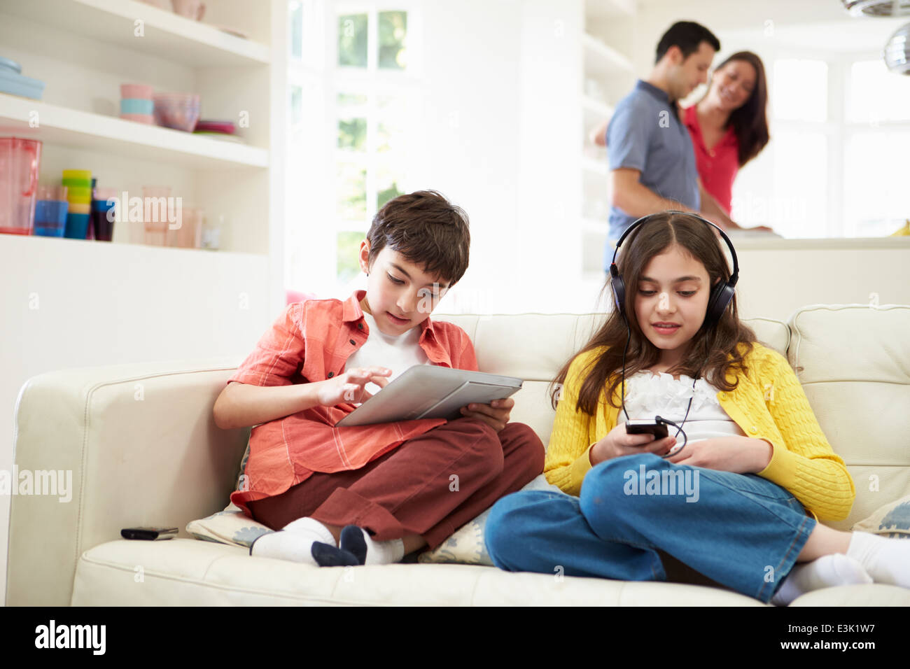 Niños jugando con dispositivos digitales como padres hacen comida Foto de stock