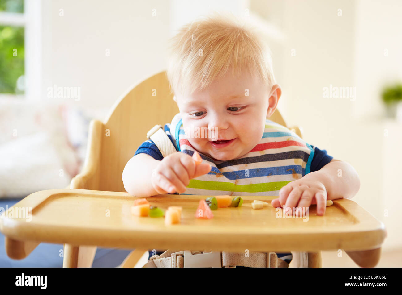 Baby Boy comer fruta en silla alta Foto de stock