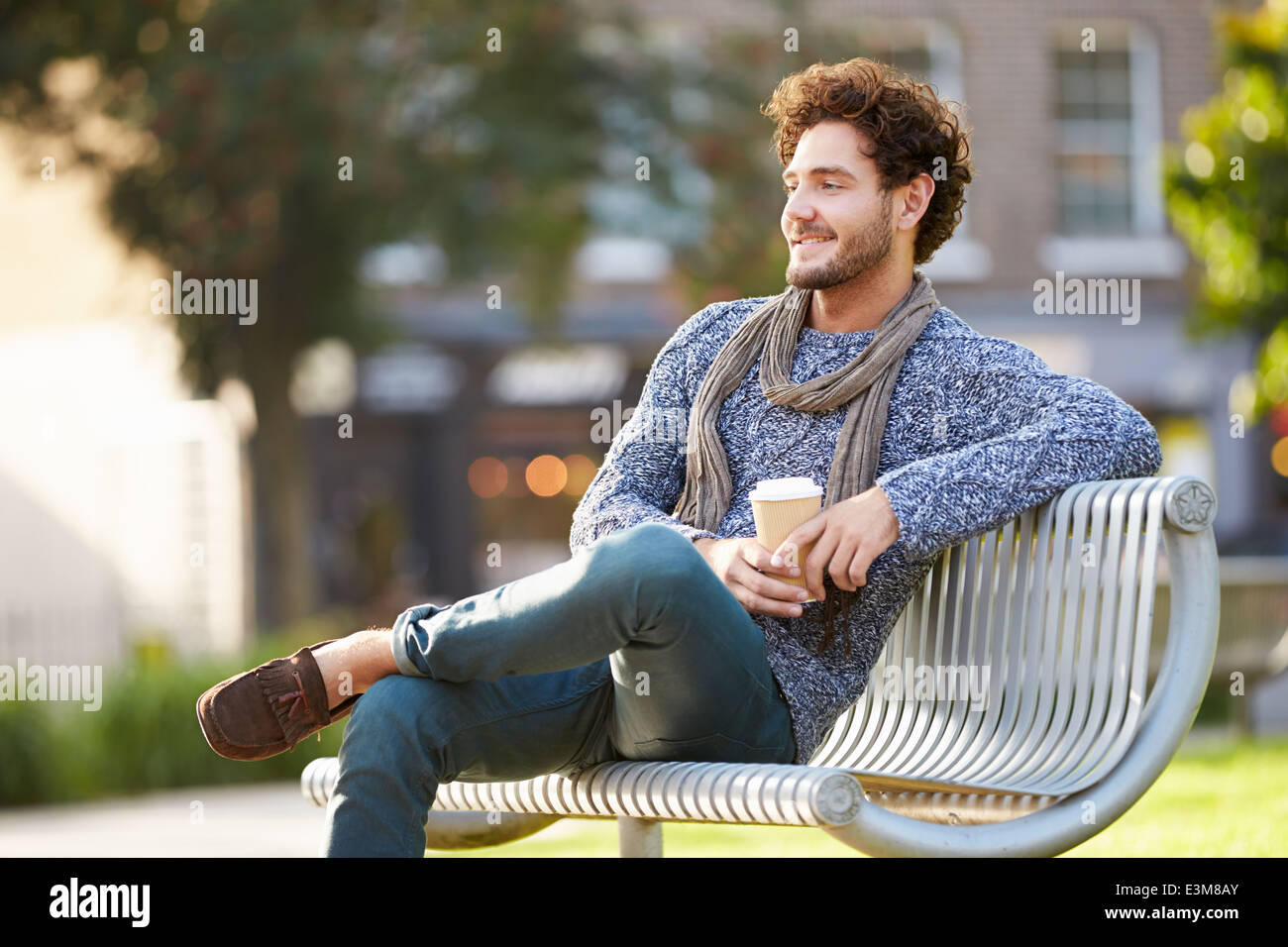 Hombre descansando en un banco de un parque con café para llevar Foto de stock