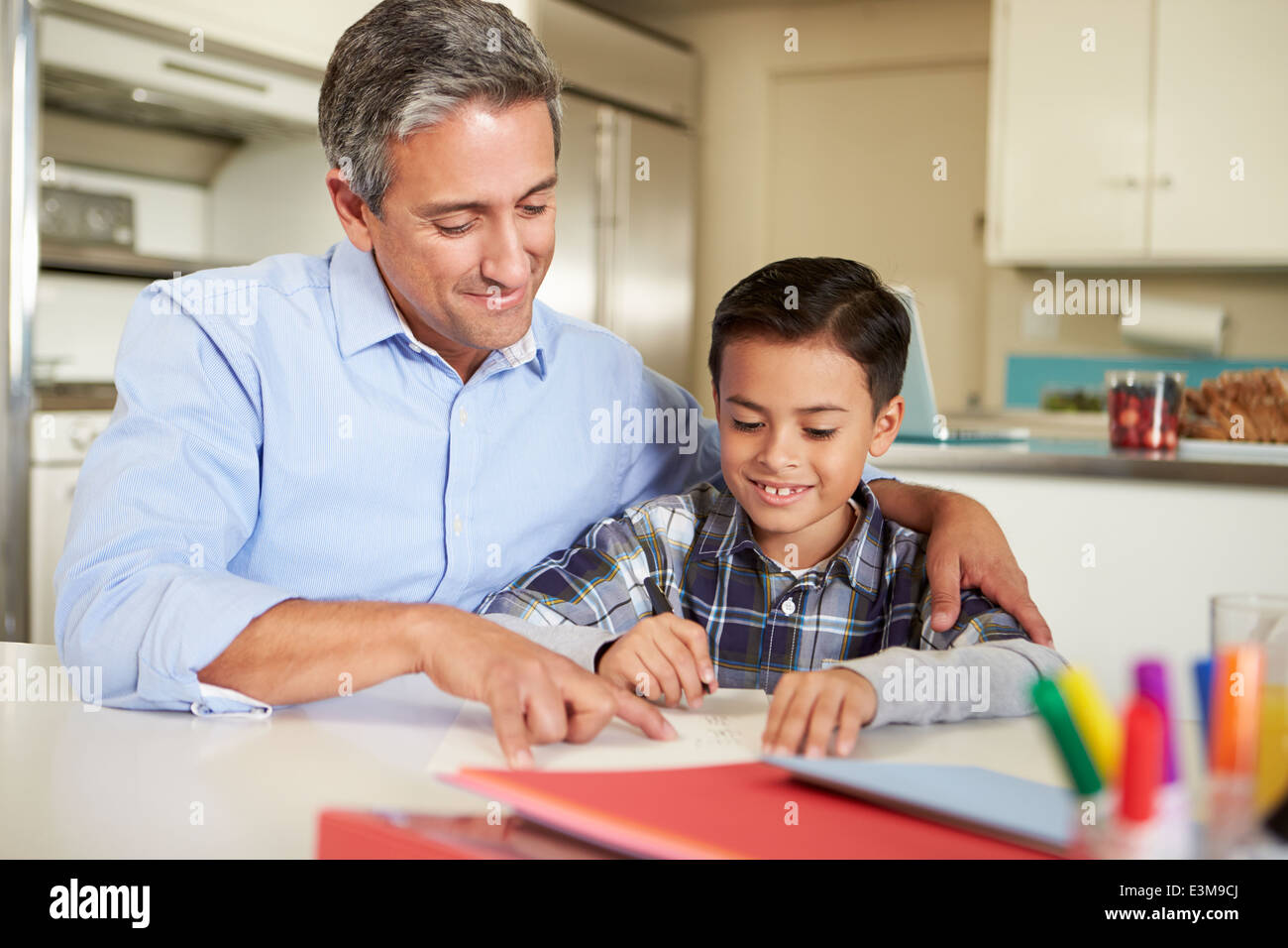 Hijo de padre hispano ayudando con las tareas en la mesa Foto de stock