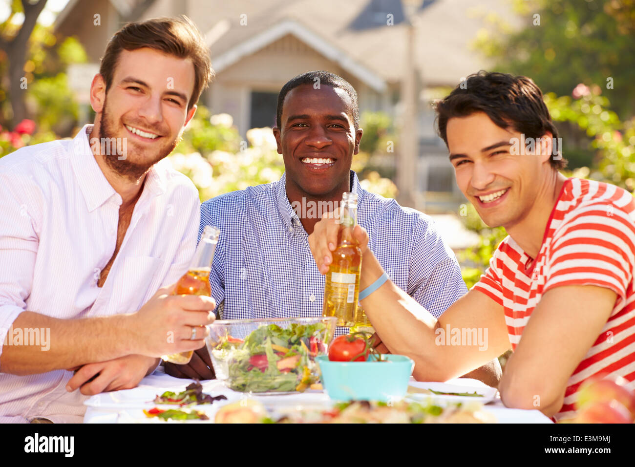 Tres hombres amigos disfrutando de comida en la fiesta al aire libre Foto de stock