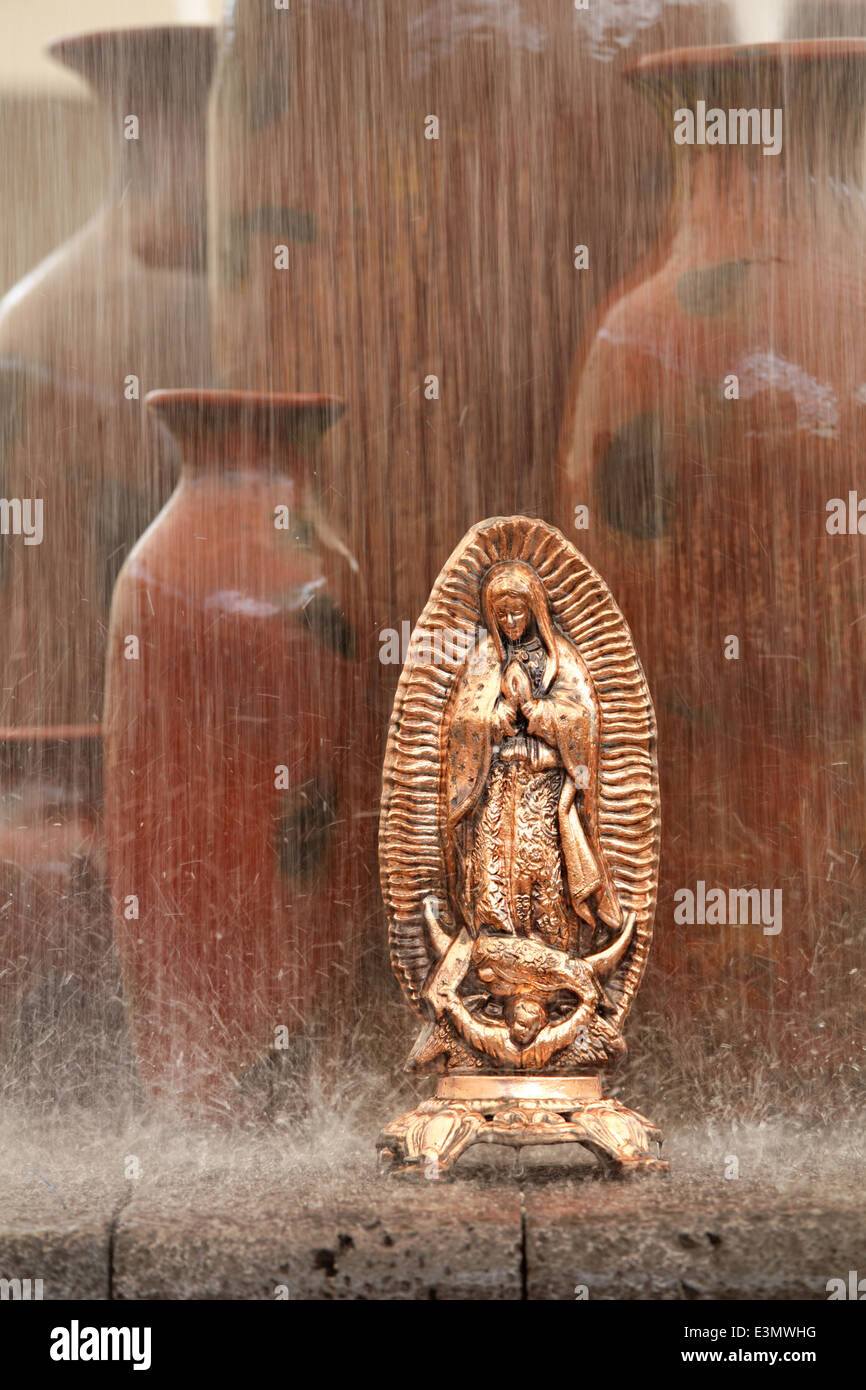 Una estatuilla de cobre virgen de Guadalupe, junto con las ollas de arcilla en una fuente, Uruapan, Michoacán, México Foto de stock