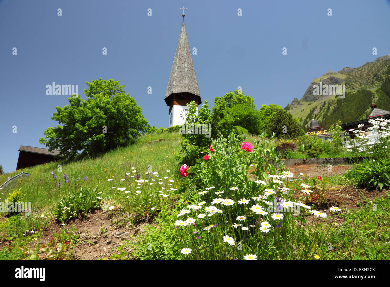Un blanco alpino un reloj y una iglesia con una torre alta y flores. Foto de stock