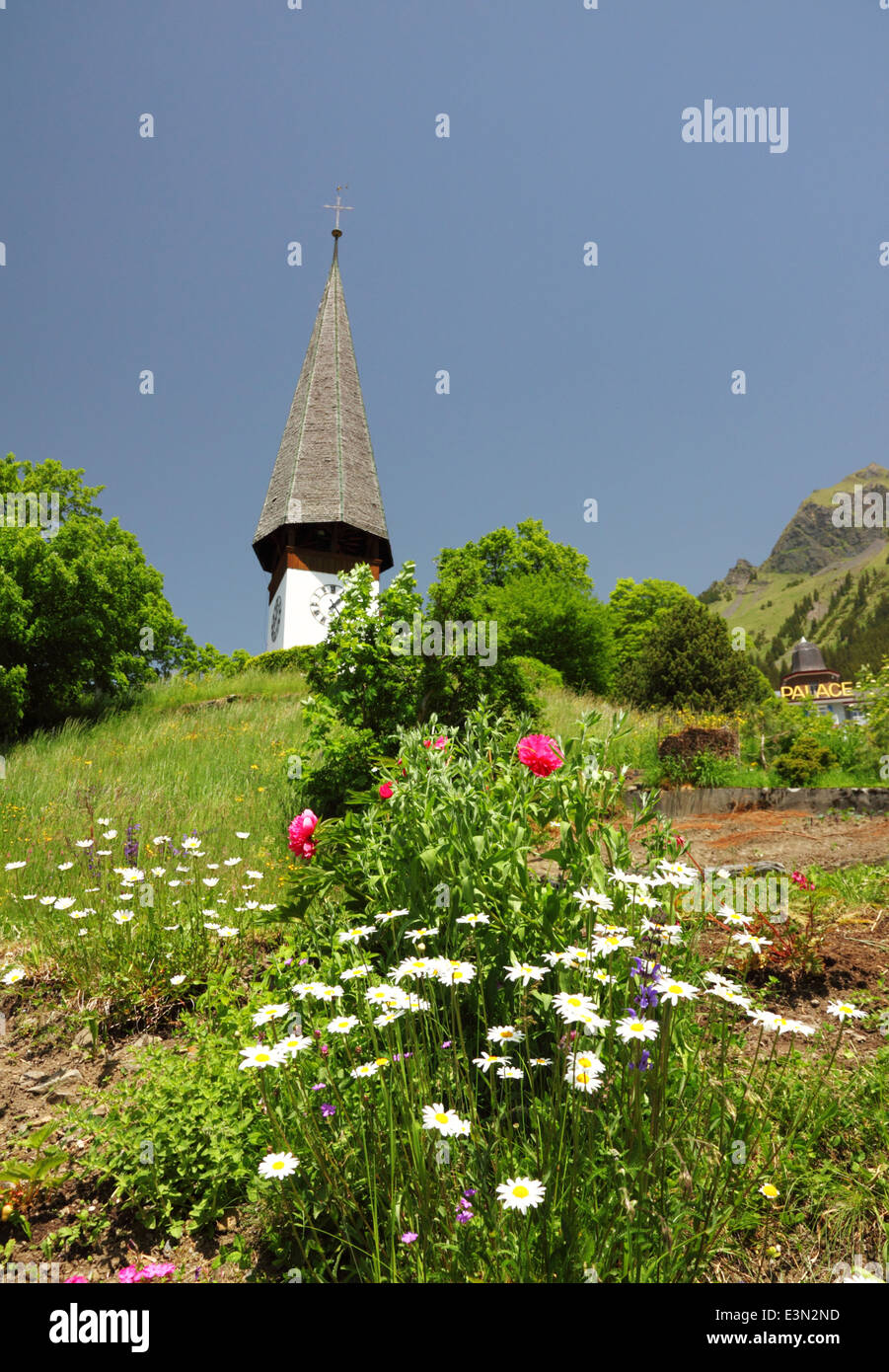 Un blanco alpino un reloj y una iglesia con una torre alta y flores. Foto de stock