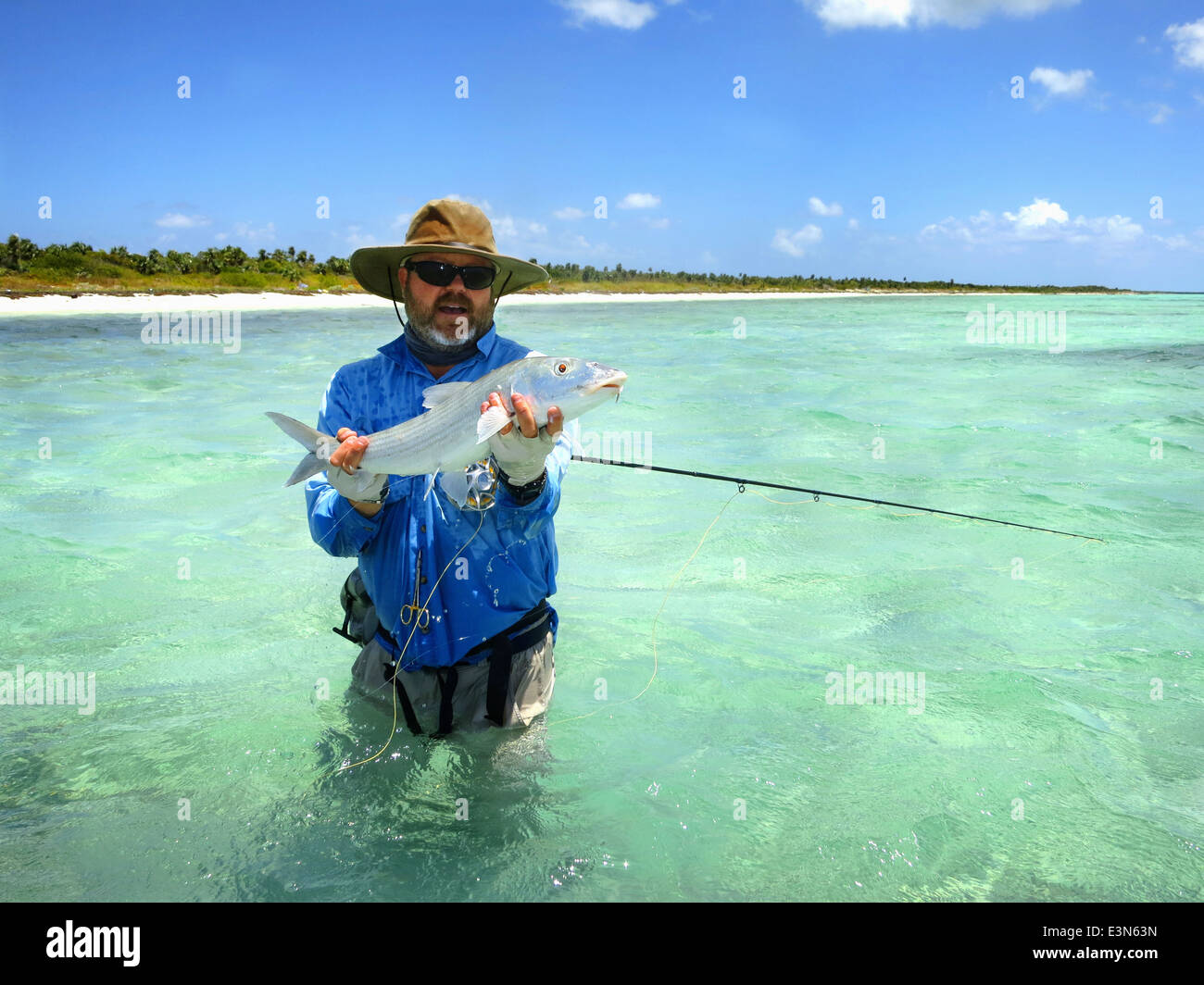 Pescador con mosca bonefish capturadas, mientras que la pesca con mosca de agua salada de vacaciones en la isla de Mayaguana en las Bahamas Foto de stock