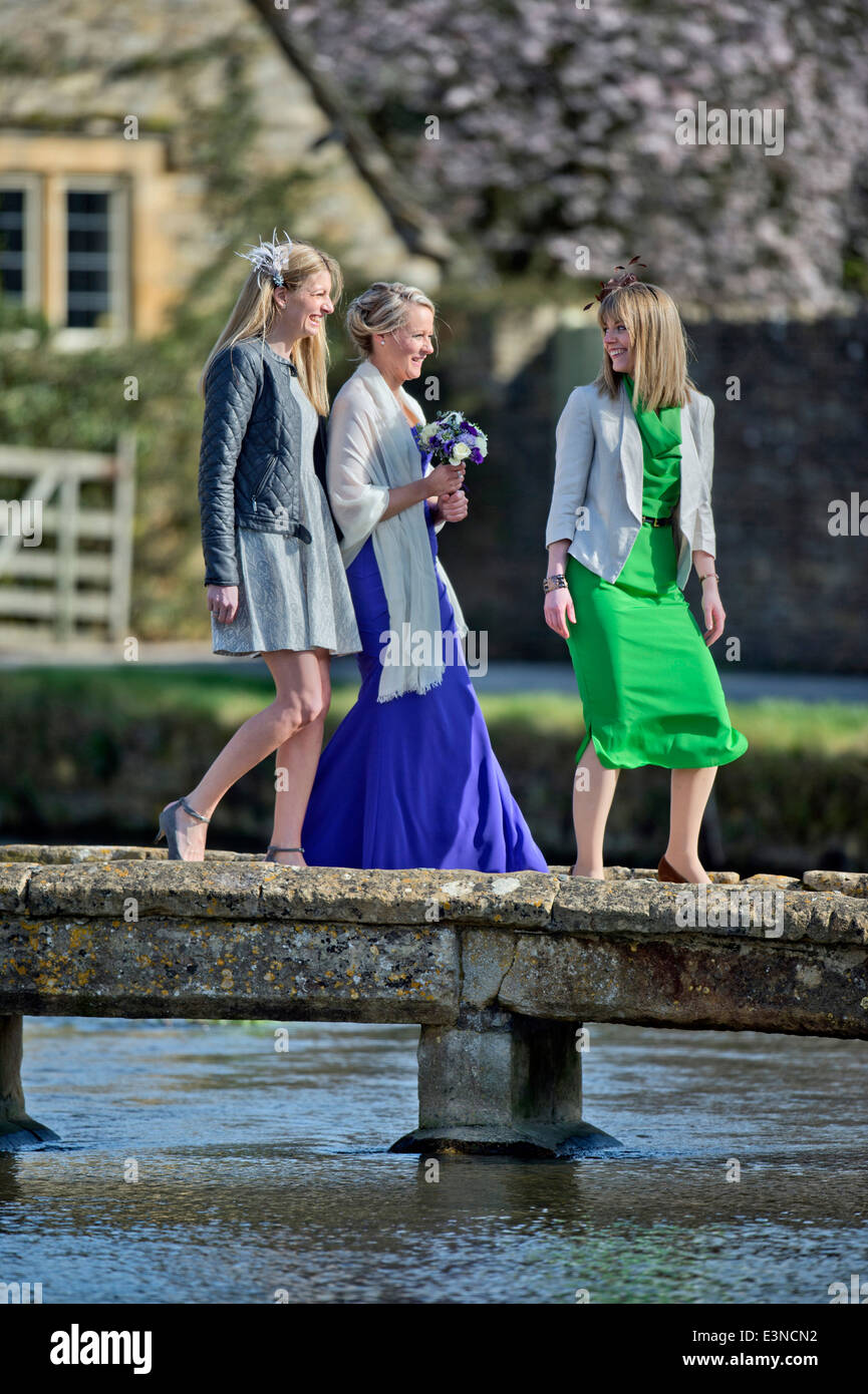 Los invitados a la boda cruzar un puente de piedra en el municipio de Lower Slaughter, Gloucestershire, Reino Unido Foto de stock
