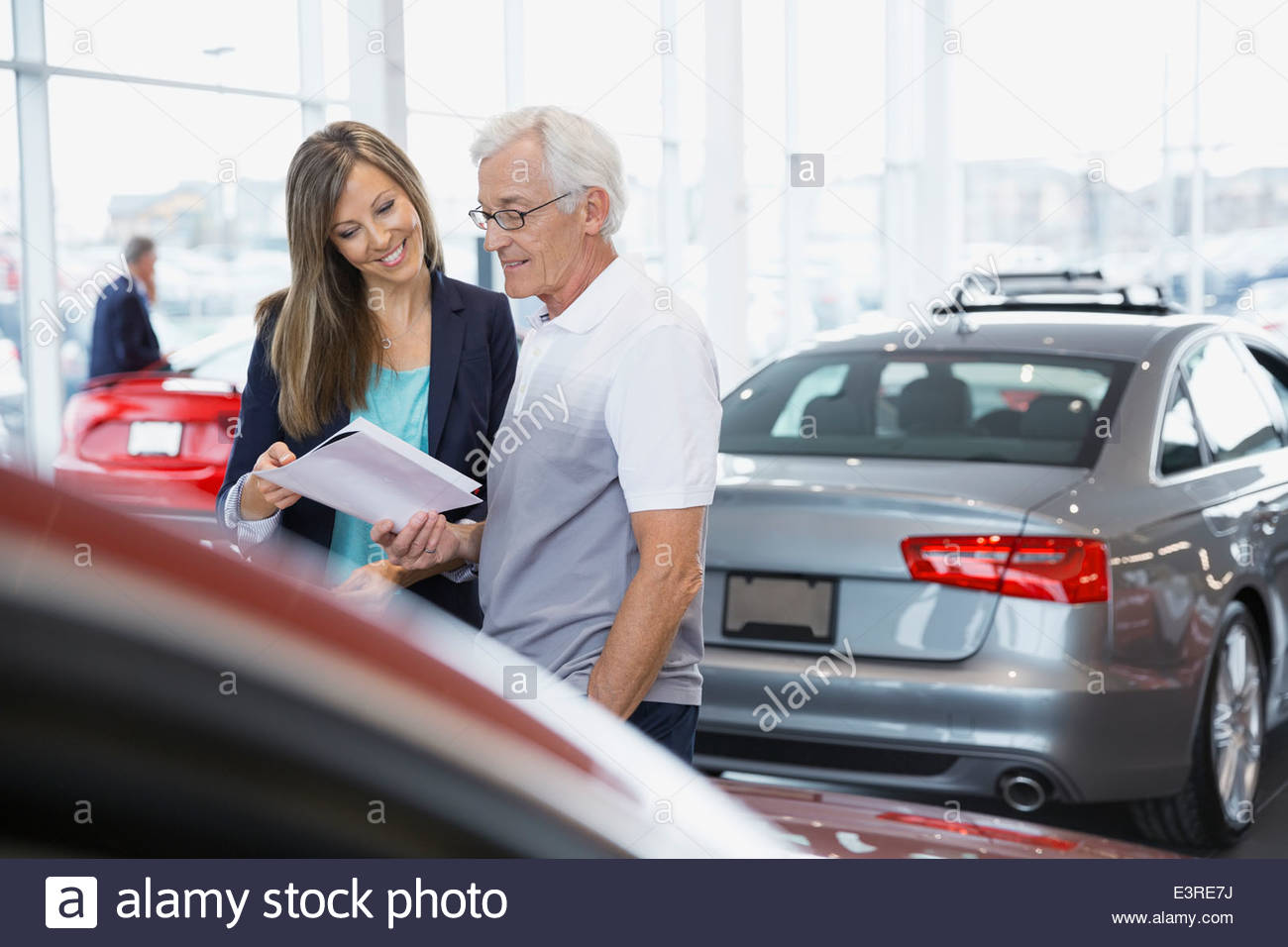 Vendedora mostrando hombre folleto en concesionario de coches showroom Foto de stock