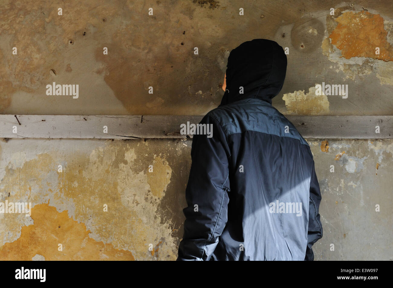 Hombre mirando la pared con textura en la casa abandonada. Foto de stock