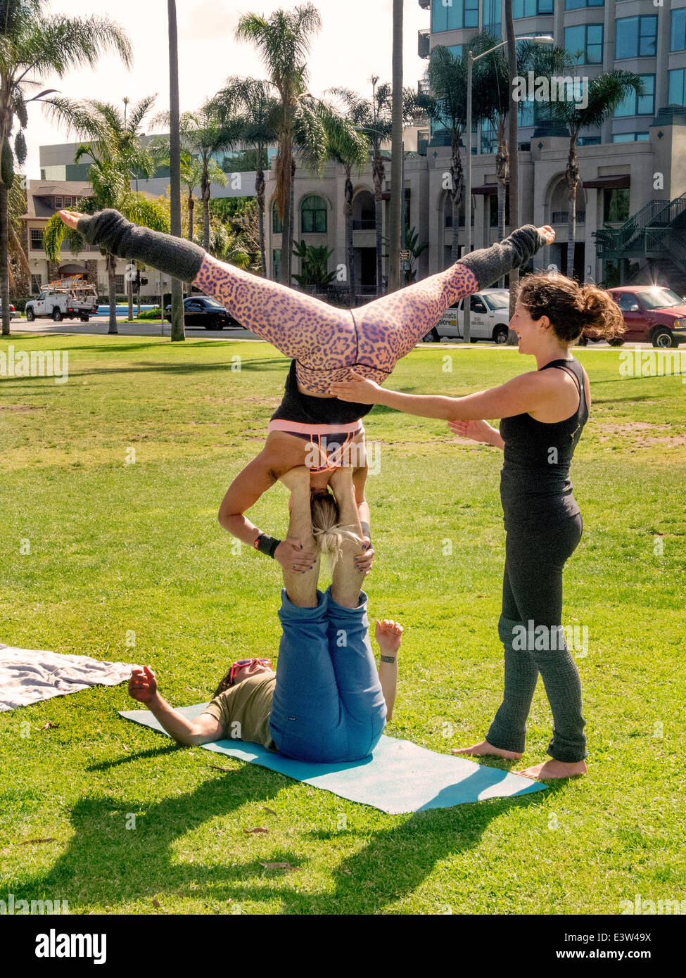 Un trío de atletas realizar Acroyoga en Balboa Park, San Diego, CA. Nota La base sobre el suelo, el flyer se celebró fuera de la tierra, y el spotter que critica a los otros dos. La actividad combina elementos del yoga, acrobacia, rendimiento y sanación arts. Foto de stock