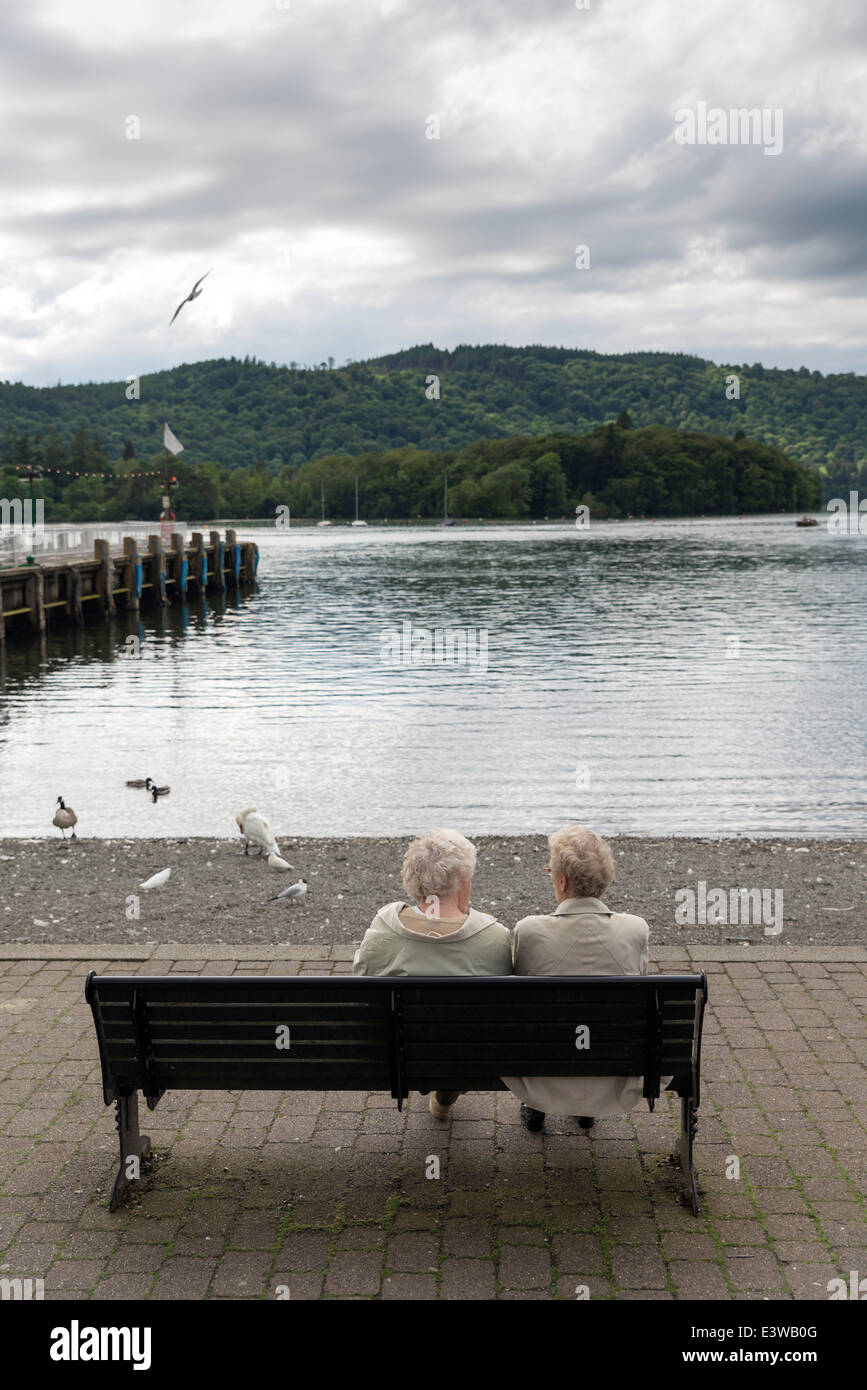 De Bowness-on-Windermere.dos ancianas irreconocible hablar sentado en un banco frente al lago Windermere, Reino Unido Foto de stock
