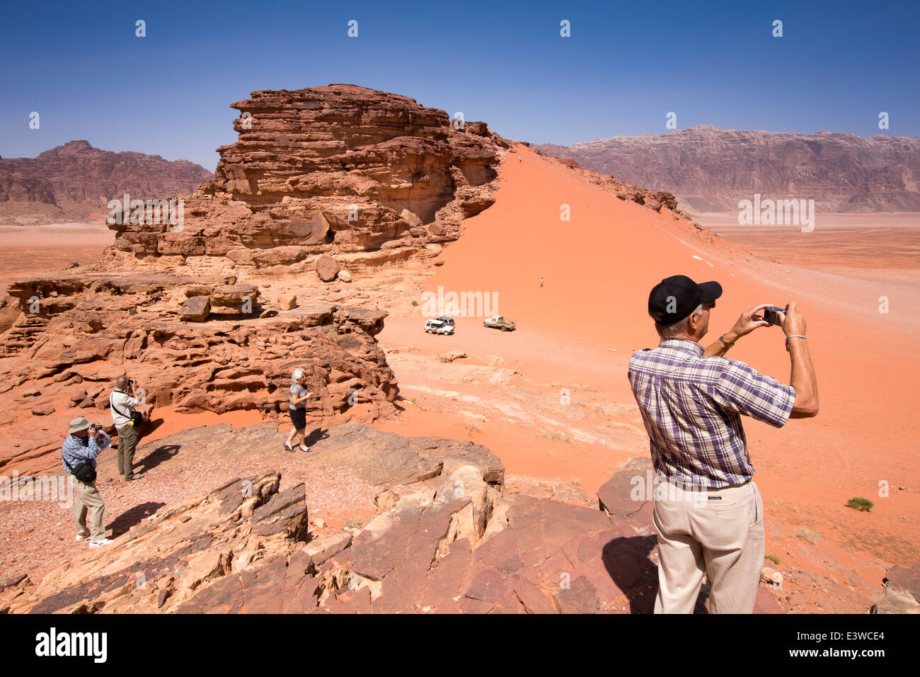 Jordania, Wadi Rum, turistas occidentales ver dunas de arena roja de afloramiento rocoso Foto de stock