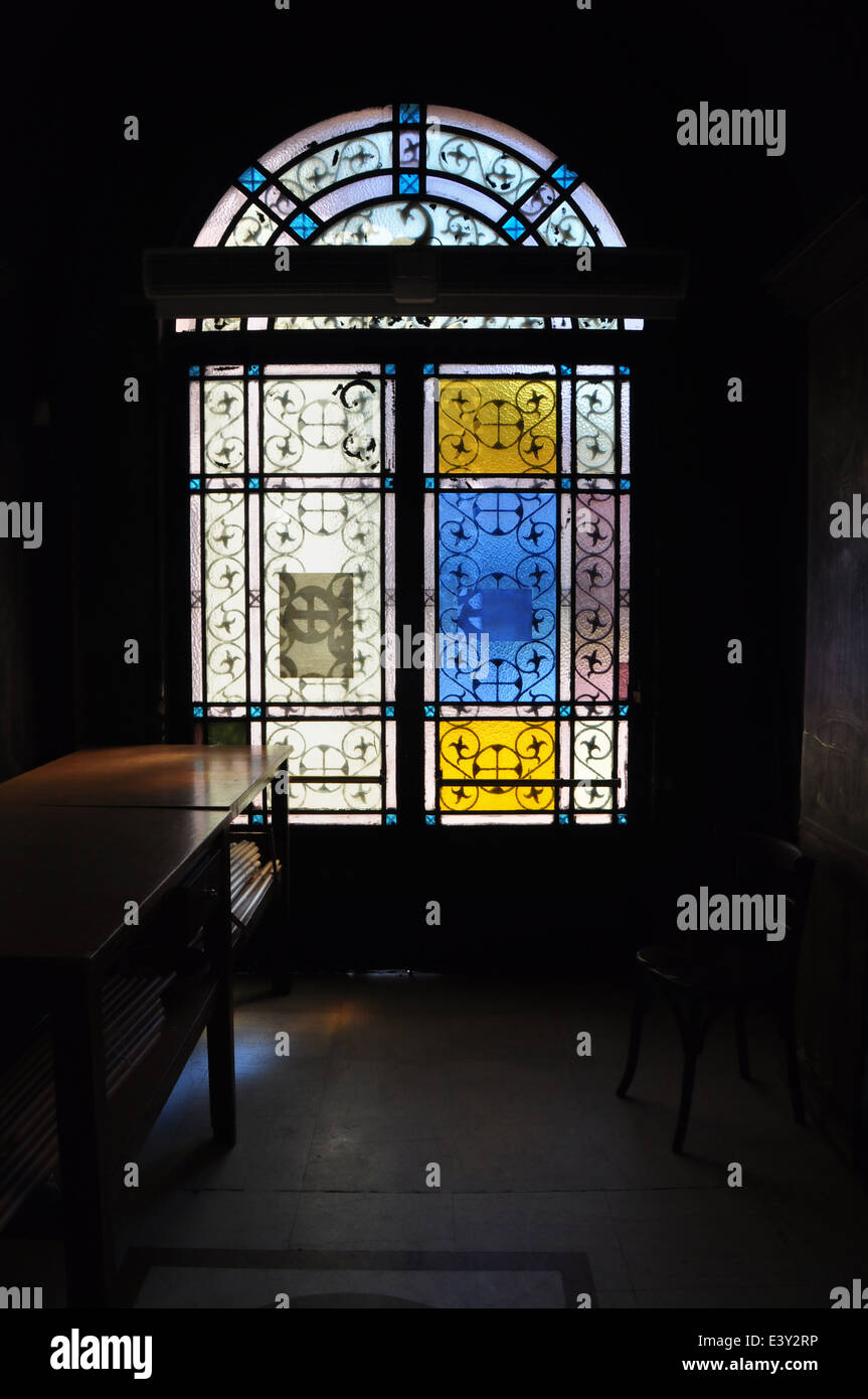 Puerta de hierro arqueados con coloridos de cristal oscuro y una silla en el interior de la iglesia. Foto de stock