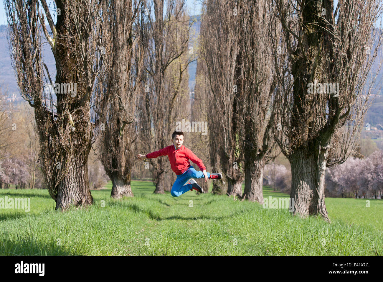 Muchacho de doce años saltando en medio del aire campo arbolada. Foto de stock