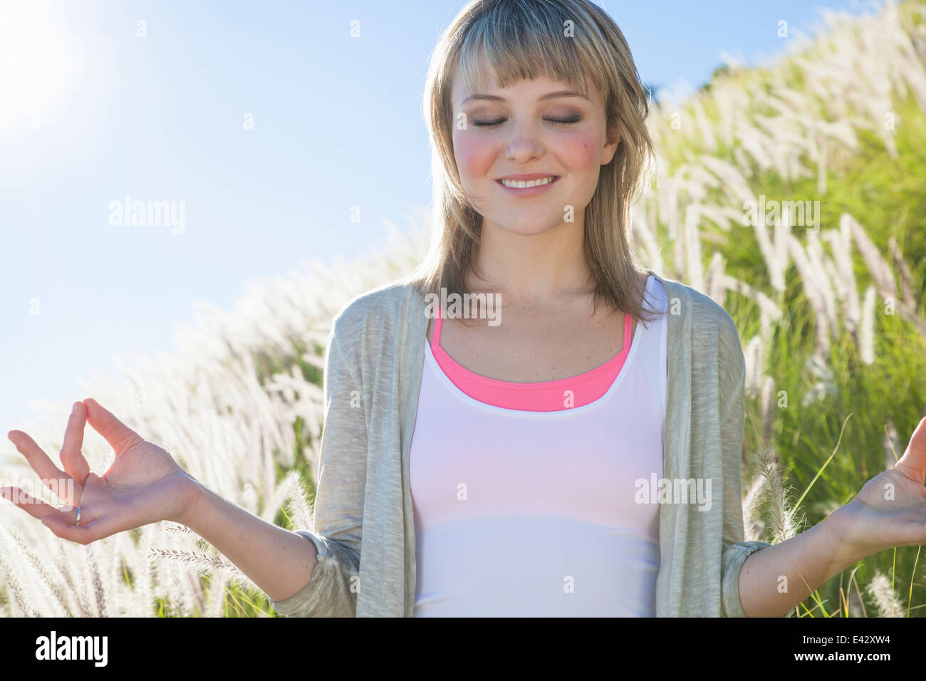 Joven mujer meditando con los ojos cerrados en el césped largo Foto de stock