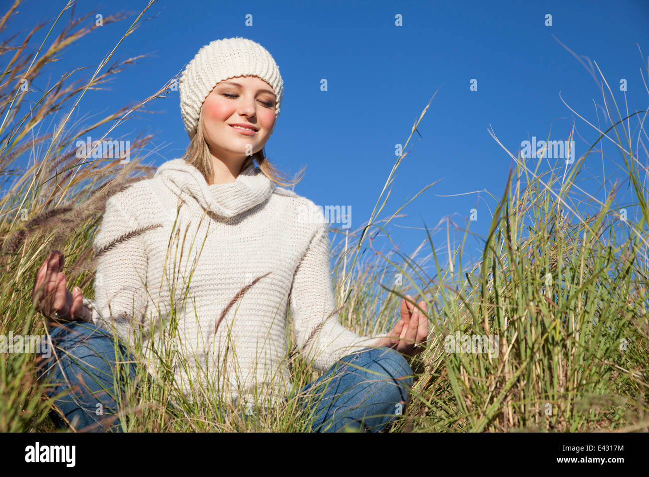 Mujer joven en posición de loto del yoga en el césped largo Foto de stock