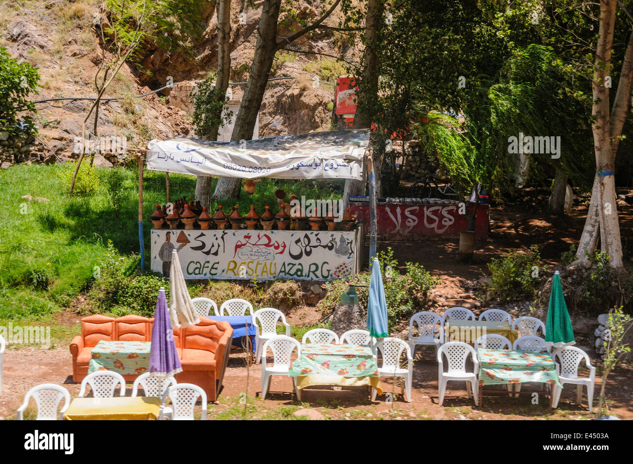 Mesas, sillas de plástico con sombrillas en los restaurantes a orillas del río Ourika, Valle de Ourika, las montañas del Atlas, Marruecos Foto de stock