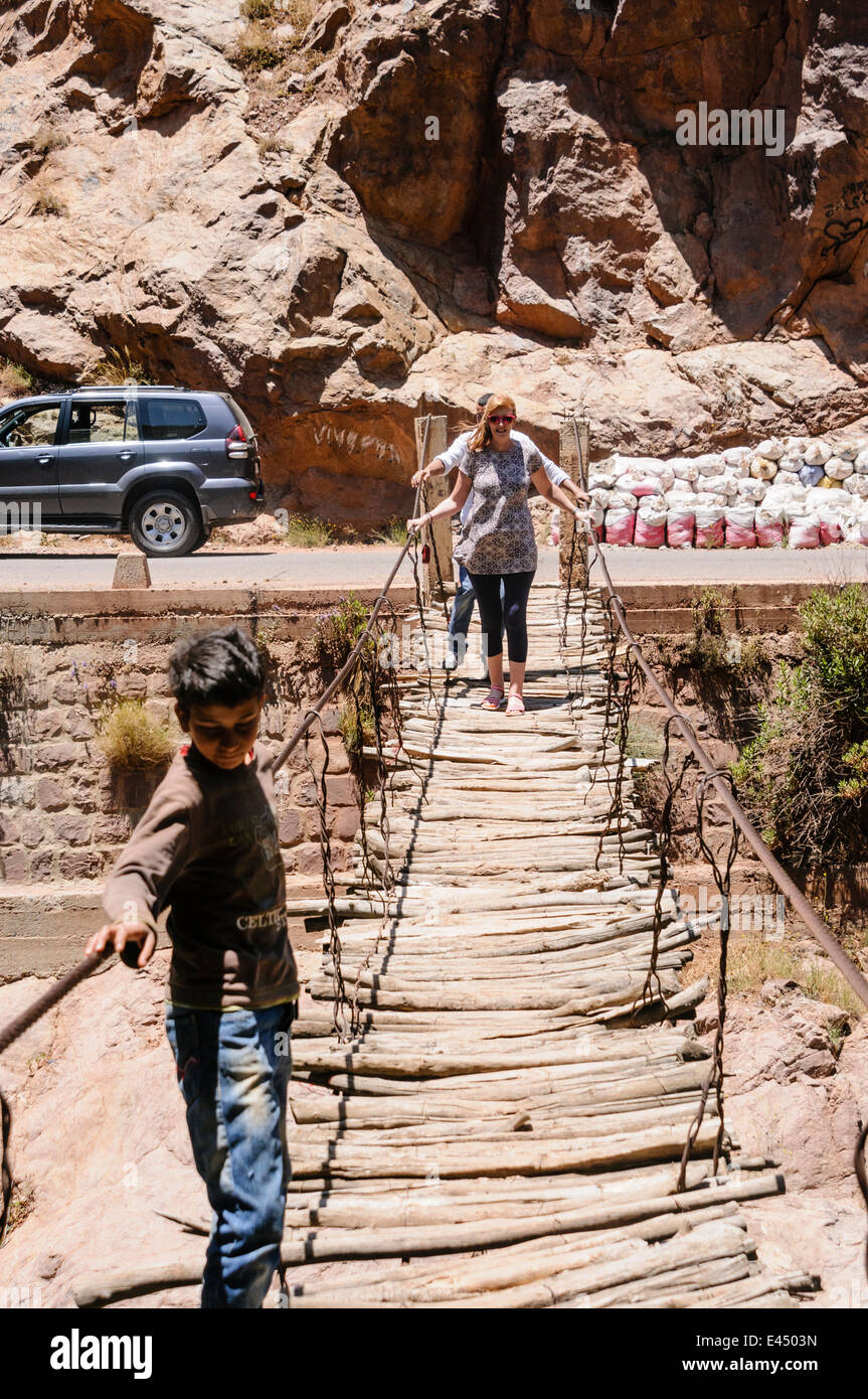 Una mujer cruza turísticos potencialmente peligrosa destartalado puente sobre el río Ourika, Valle de Ourika, las montañas del Atlas, Marruecos Foto de stock