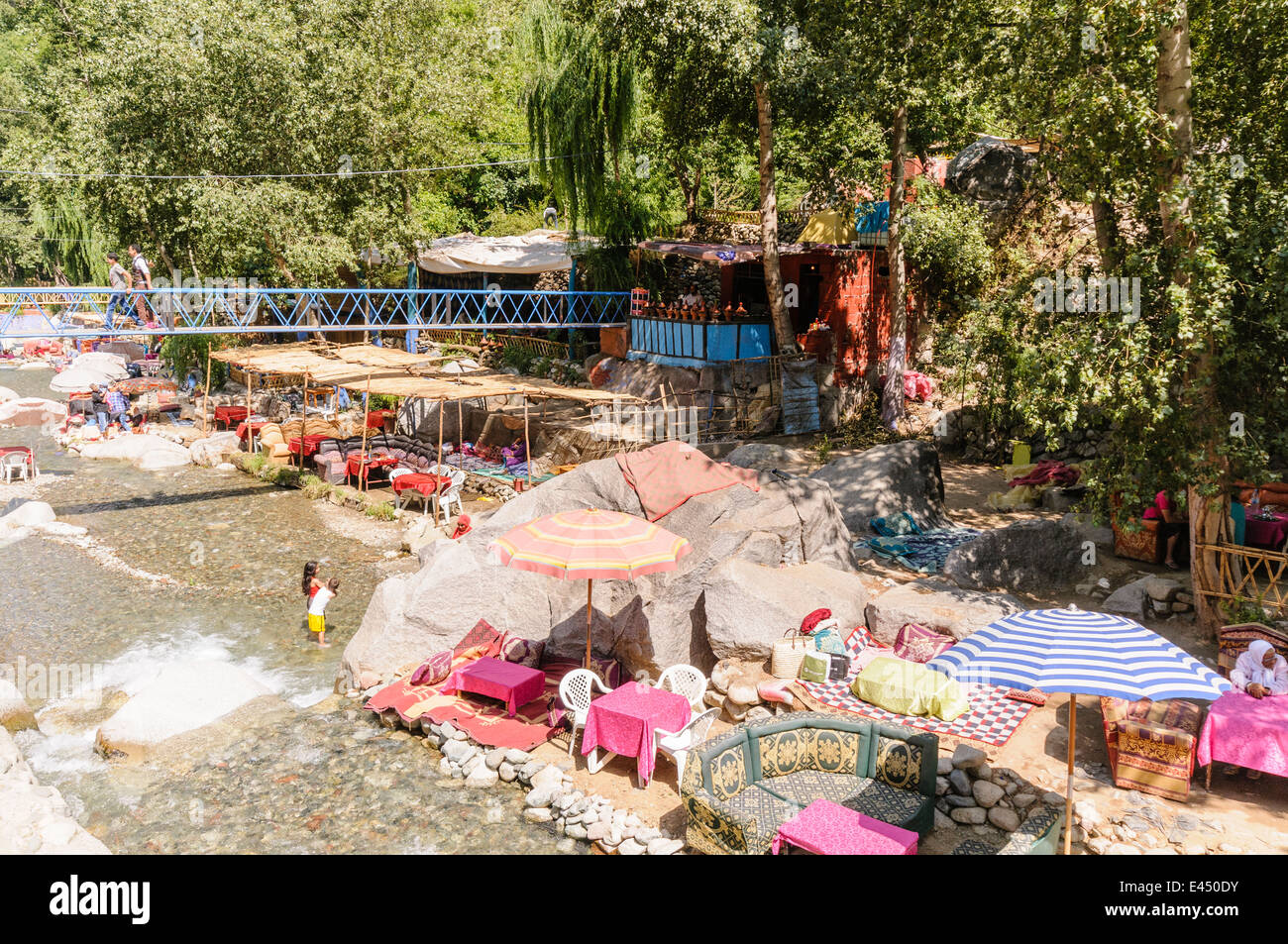 Mesas, sillas de plástico con sombrillas en los restaurantes a orillas del río Ourika, Valle de Ourika, las montañas del Atlas, Marruecos Foto de stock