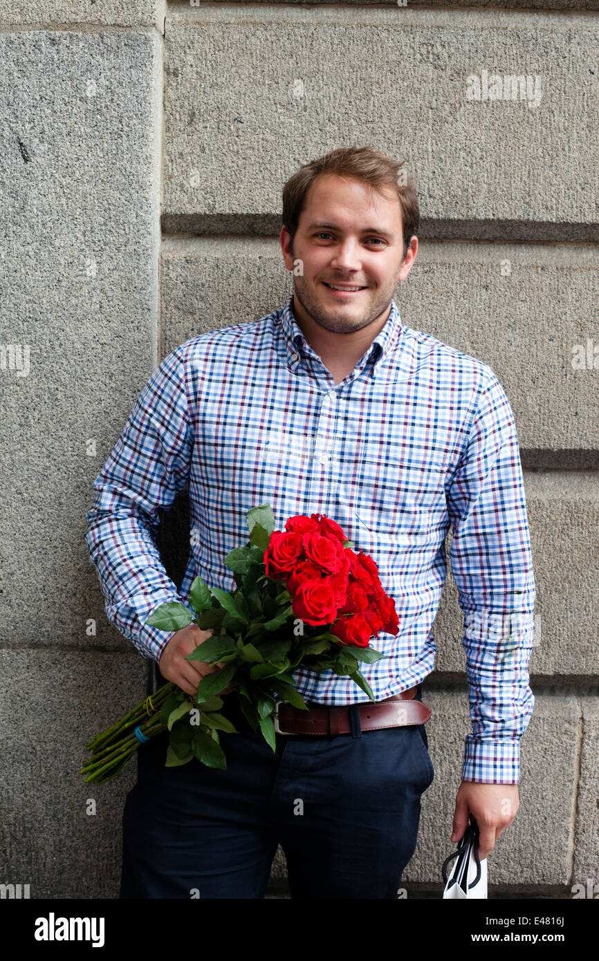 Un hombre espera para ir a una cita con un ramo de rosas rojas en la plaza, el mercado de Covent Garden, Londres, Reino Unido. Foto de stock