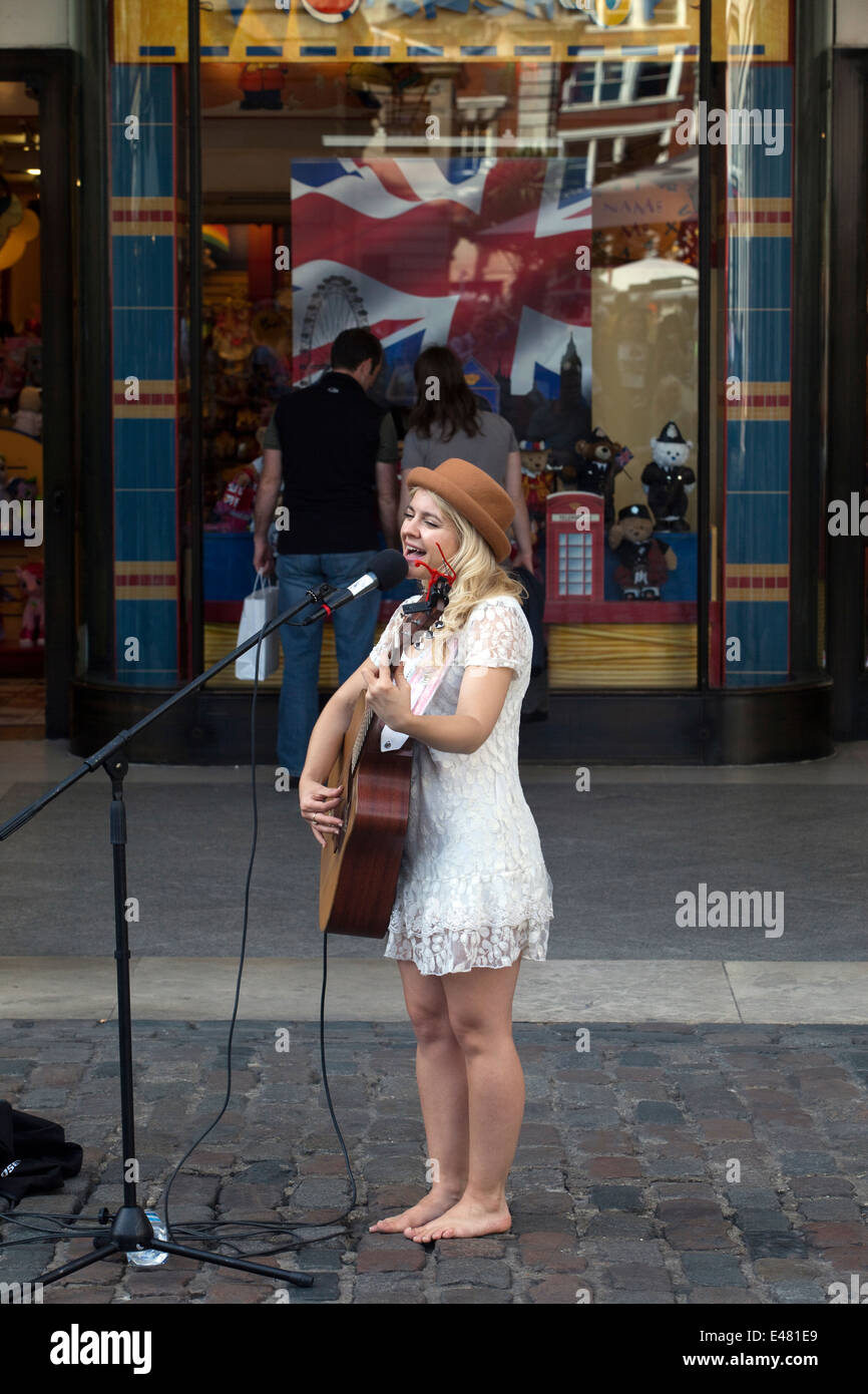 Una mujer músico callejero canta y toca la guitarra a una multitud en el mercado de Covent Garden, Londres, Reino Unido. Foto de stock
