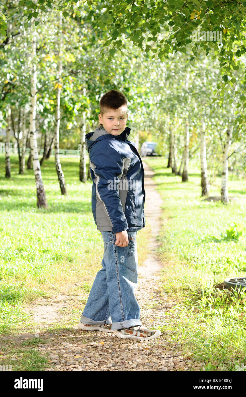 Kid niño un parque de árboles de verano fresco verde chaqueta cortavientos pathway 8 años jeans caminando hablando de infancia caucasian Foto de stock