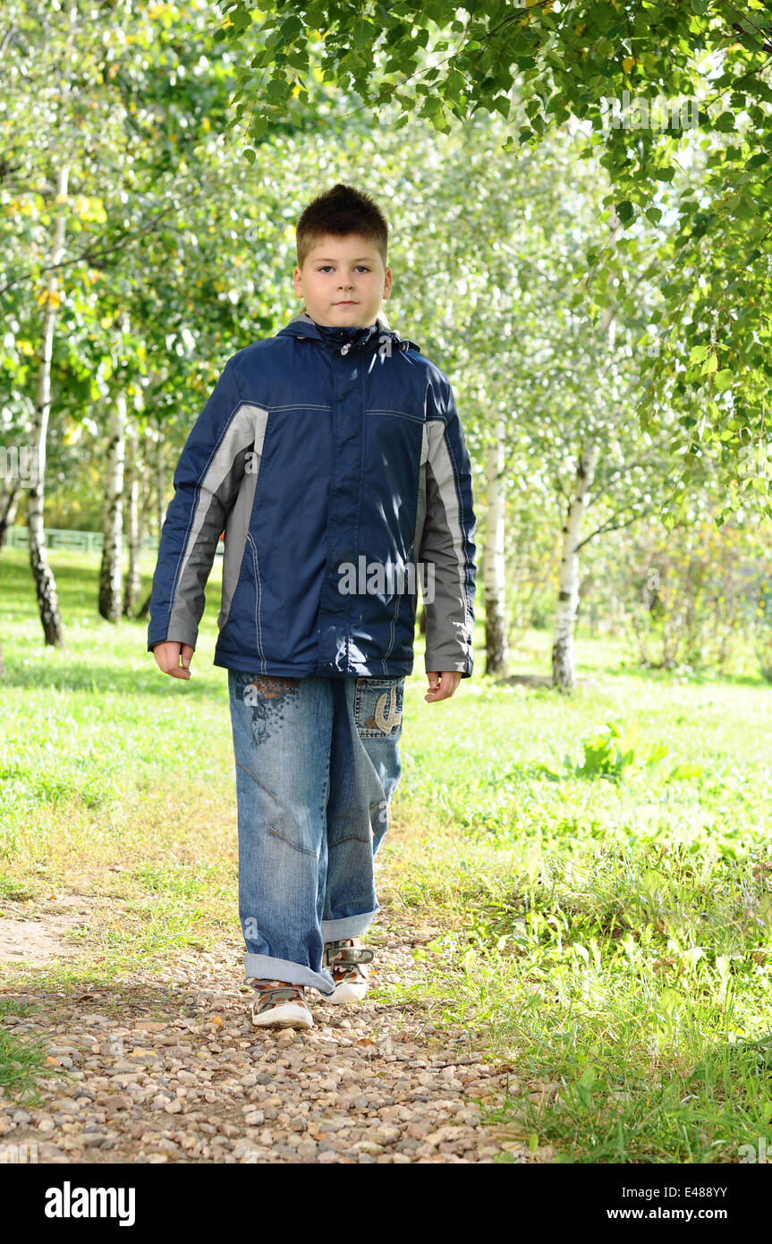 Kid niño un parque de árboles de verano fresco verde chaqueta cortavientos pathway 8 años jeans caminando hablando de infancia caucasian Foto de stock