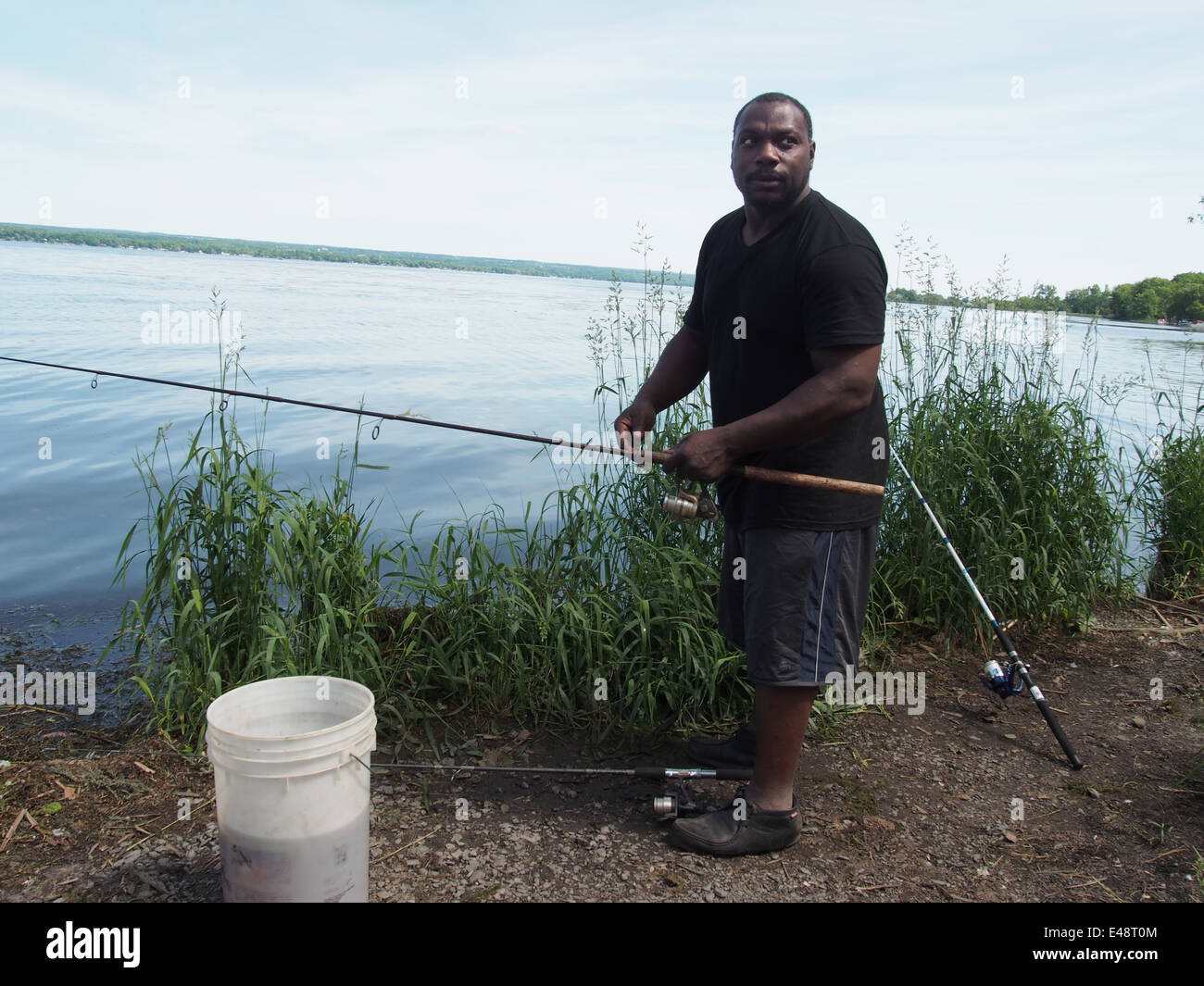Hombre afroamericano la pesca en el lago Cayuga, Nueva York, EEUU, 15 de junio de 2014, © Katharine Andriotis Foto de stock