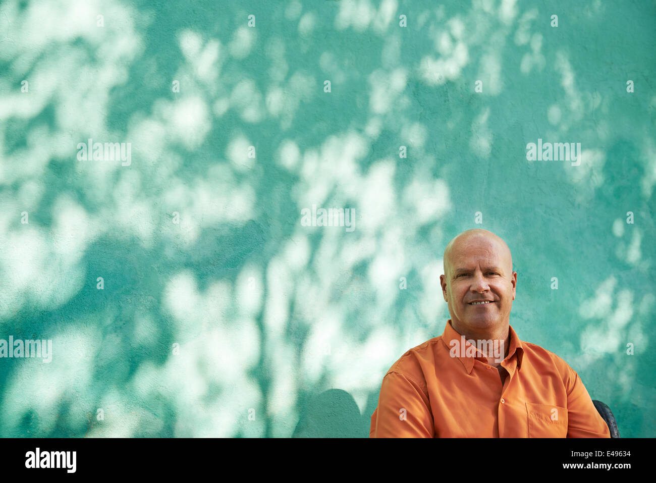 Retrato del hombre caucásico madura con camiseta naranja sentado en el parque y mirando a la cámara con expresión feliz Foto de stock