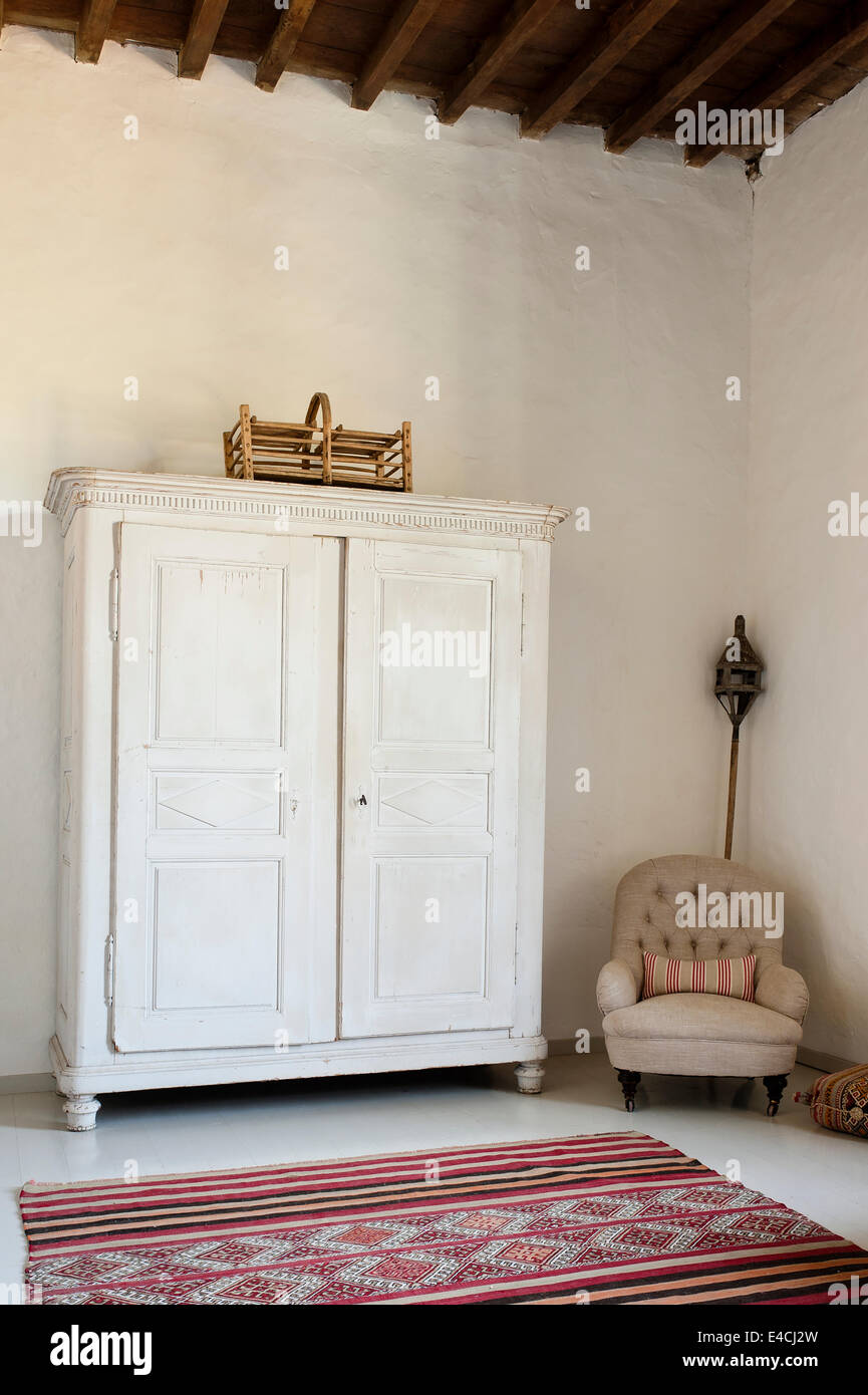 Armario de madera blanca en amplias habitaciones con techos altos, seguro sillón y alfombra marroquí Foto de stock