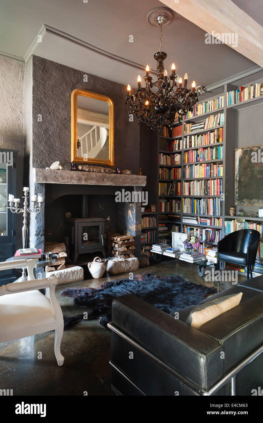 Sala de estar en un palacio restaurado con construido en estantes de libros, Corbusier sofá de cuero negro y cromo candalabra,woodburner fro Foto de stock