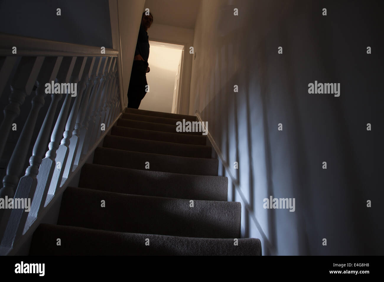 Silueta de un hombre apoyado contra la pared en la parte superior de una escalera, las sombras proyectadas en las paredes de la luz debajo. Foto de stock