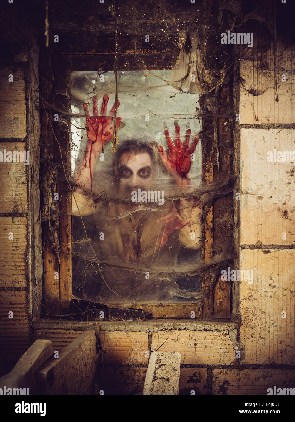 Foto de un zombie fuera de una ventana que está cubierto de sangre, spiderwebs y suciedad. Foto de stock