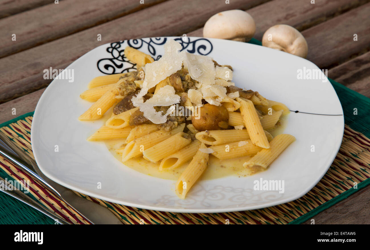 Pasta con champiñones picados y queso parmesano en la placa cuadrada blanca Foto de stock