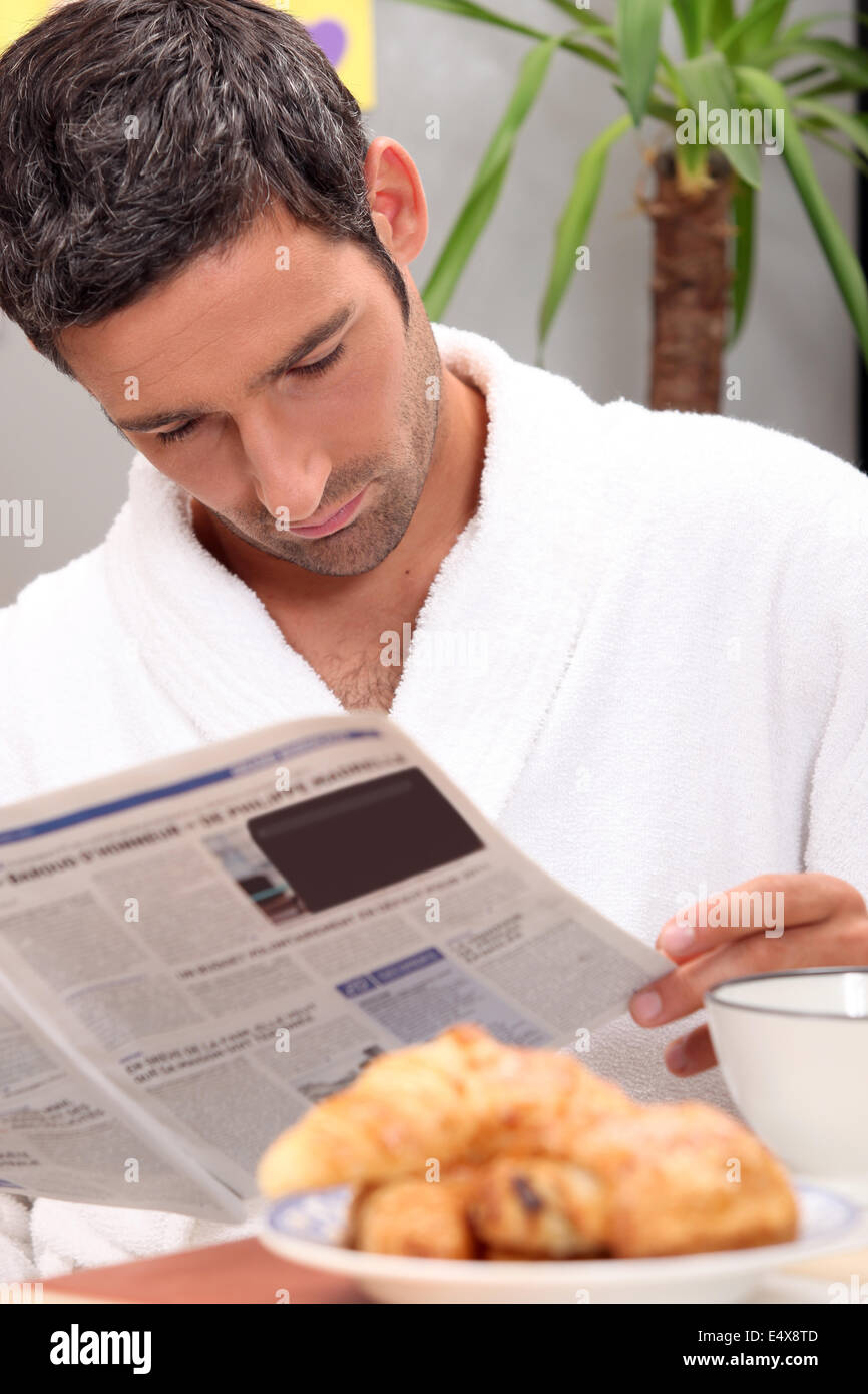 Hombre leyendo un diario durante el desayuno Foto de stock