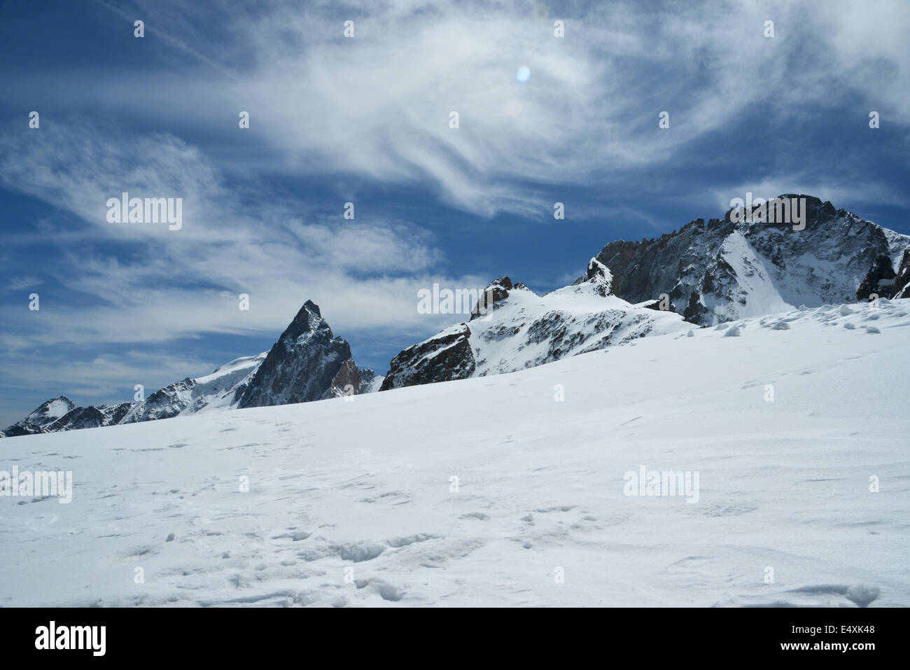 El sol brillante resplandece sobre la nitidez del blanco de la nieve en la cima de una montaña alpina bajo un cielo azul profundo Foto de stock