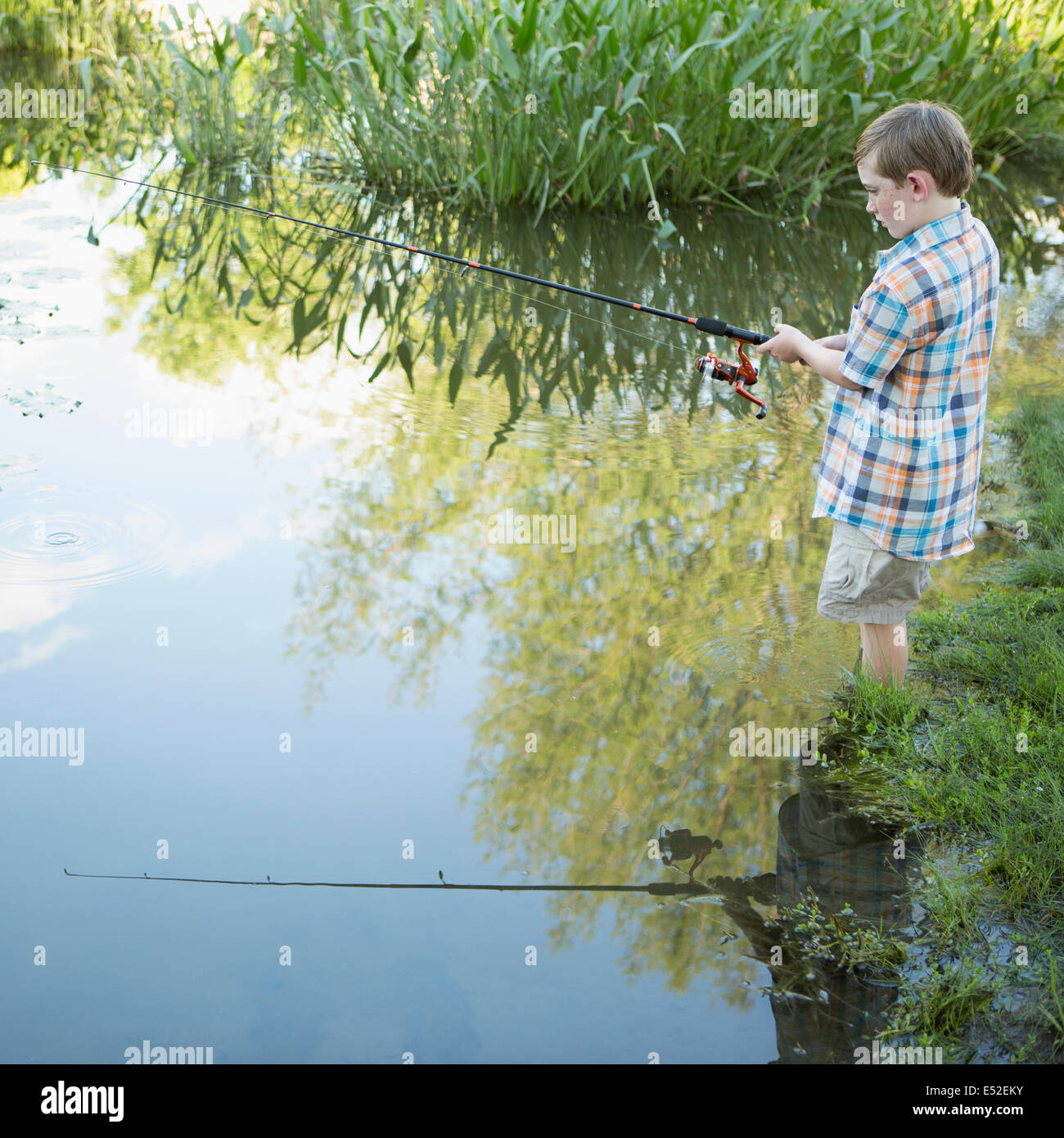 Un joven parado en agua pesca con una varilla. Foto de stock