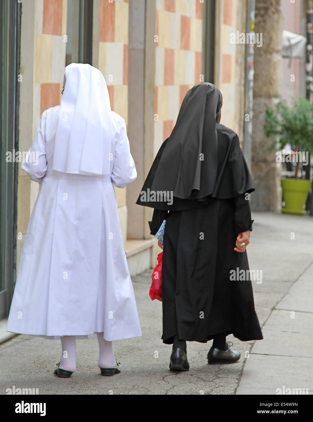 Dos viejas hermanas con traje negro y vestido blanco caminando en la ciudad Foto de stock