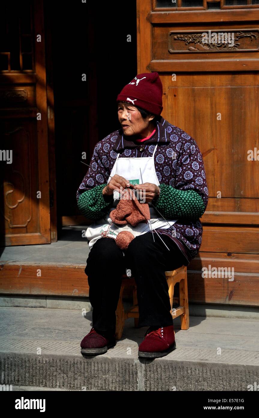 XIN XING ZHEN, CHINA: mujer vistiendo un calcetín viejo gorro de punto y zapatos no coincidentes knits delante de una puerta de celosía de madera Foto de stock