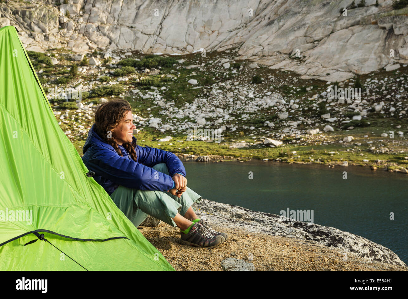 Mujer de mochilero camper sentado junto a su carpa viendo la puesta de sol por la evolución del Lago Foto de stock