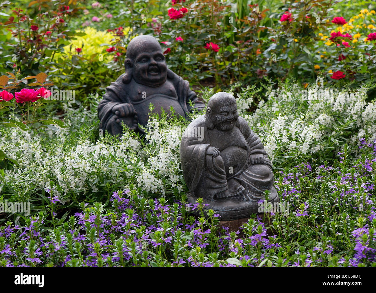 Casa jardín de flores en plena floración con la escultura de Buda. Foto de stock