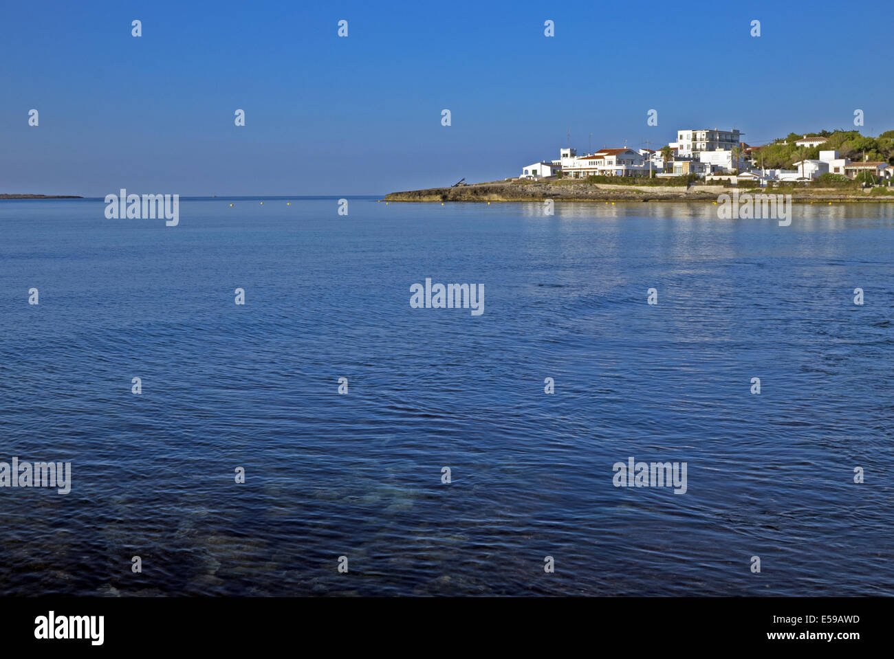 Temprano en la mañana vista del tradicional pueblo de Punta Prima, Menorca, España. Claro azul del cielo despejado y el azul del mar Mediterráneo. Foto de stock