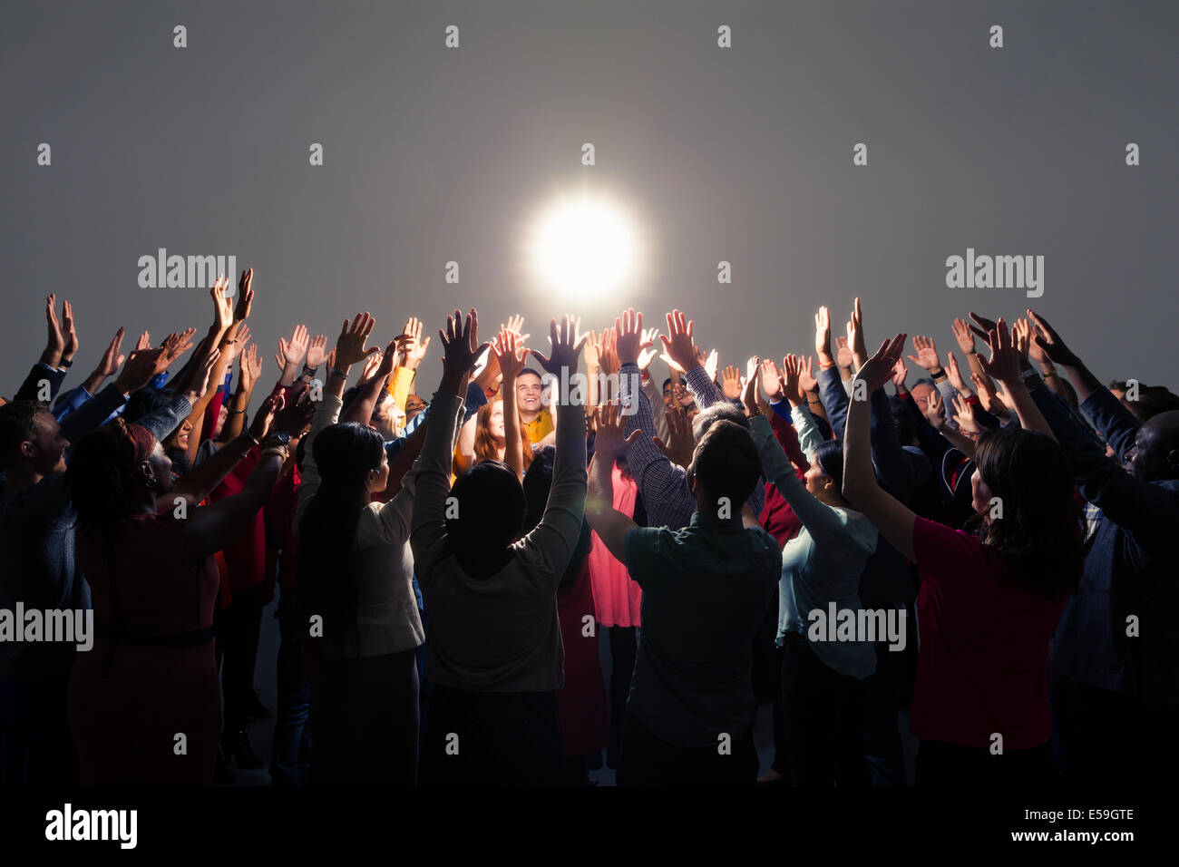 Clientela diversa con los brazos levantados alrededor de luz brillante Foto de stock