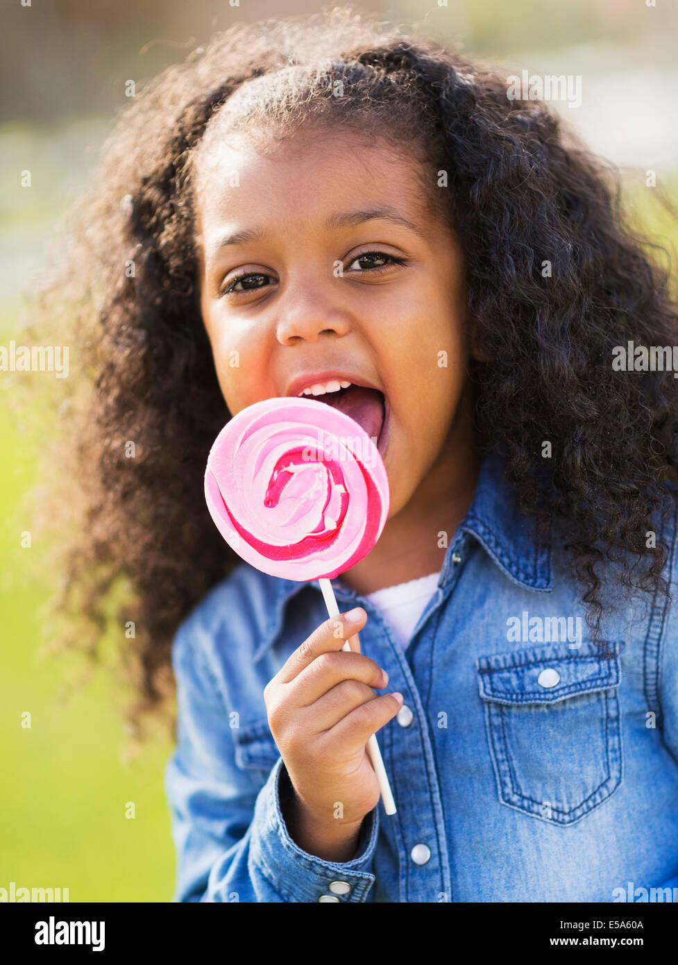 Raza mixta chica lamiendo lollipop afuera Foto de stock
