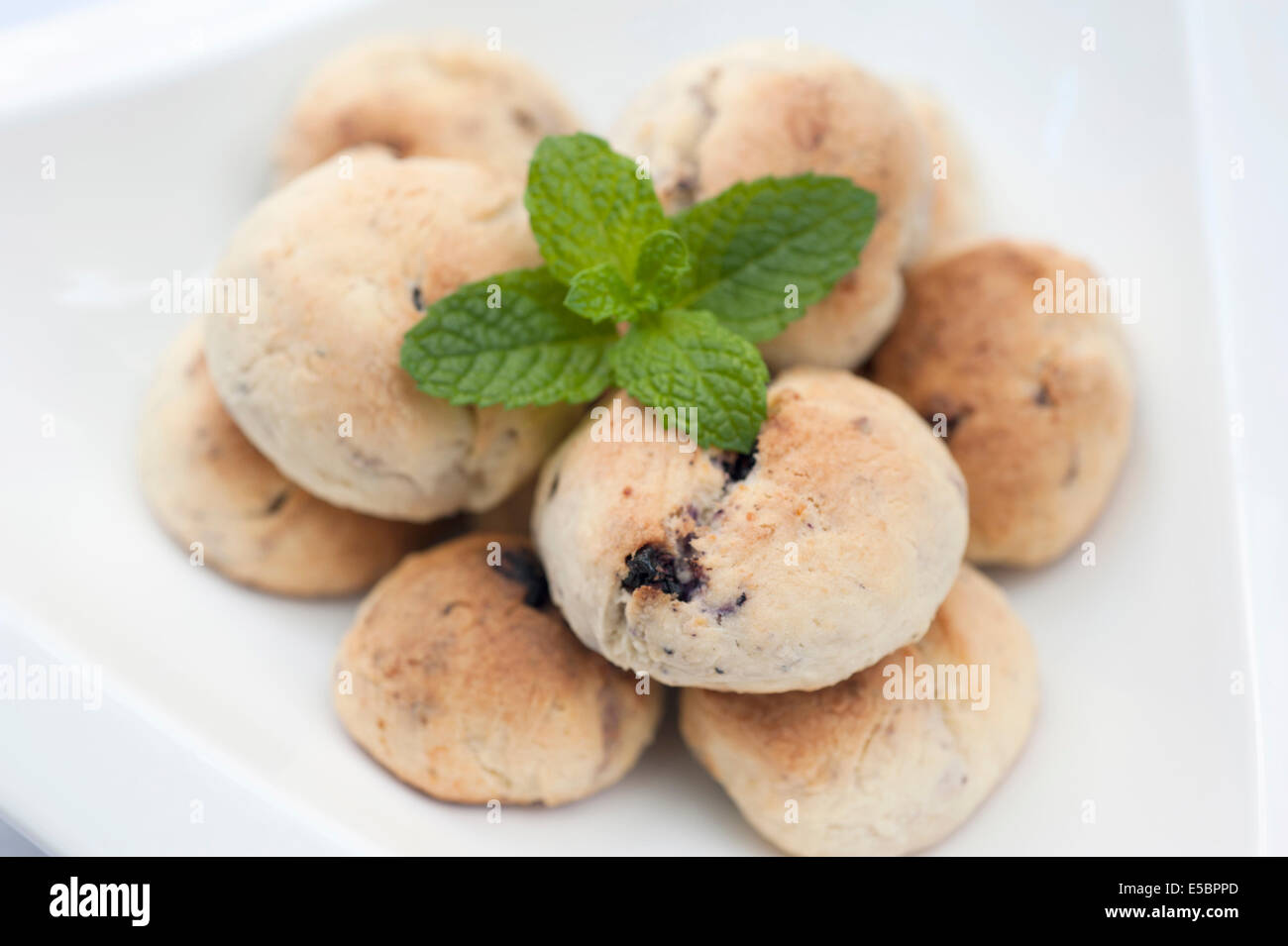 Blueberry galletas artesanales con menta en la parte superior y en un recipiente blanco sobre un fondo blanco. Foto de stock