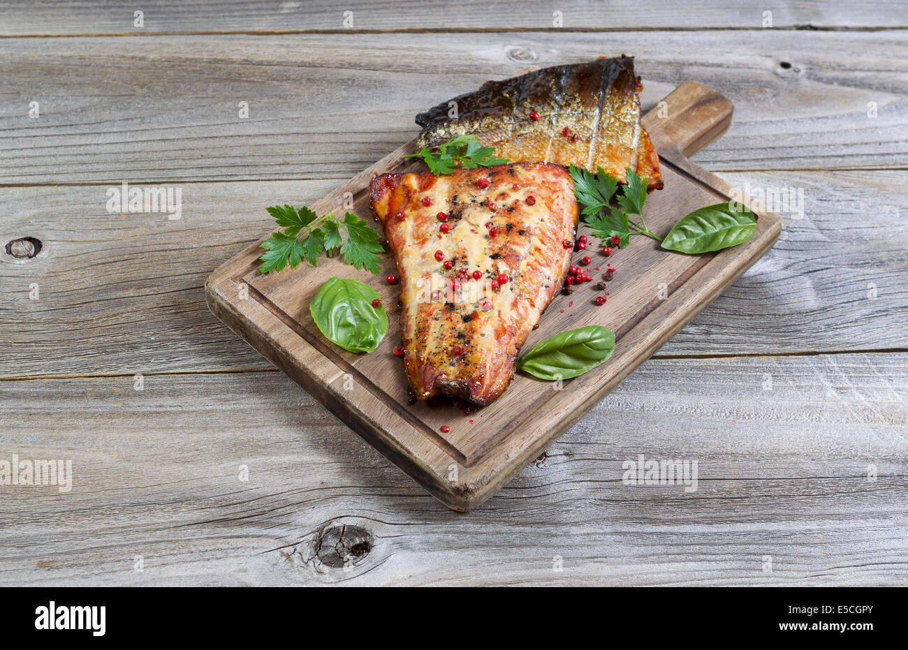 Vista horizontal de filetes de salmón ahumado, recién salida de la cocina, con aliño en servir a bordo con madera rústica debajo Foto de stock