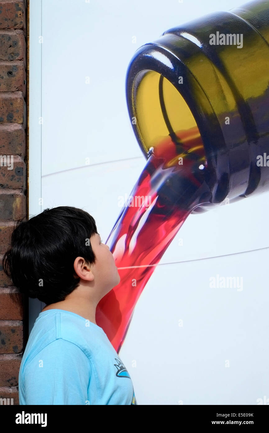 Joven posando delante de un póster fingiendo beber vino vertiendo de botella foto Foto de stock