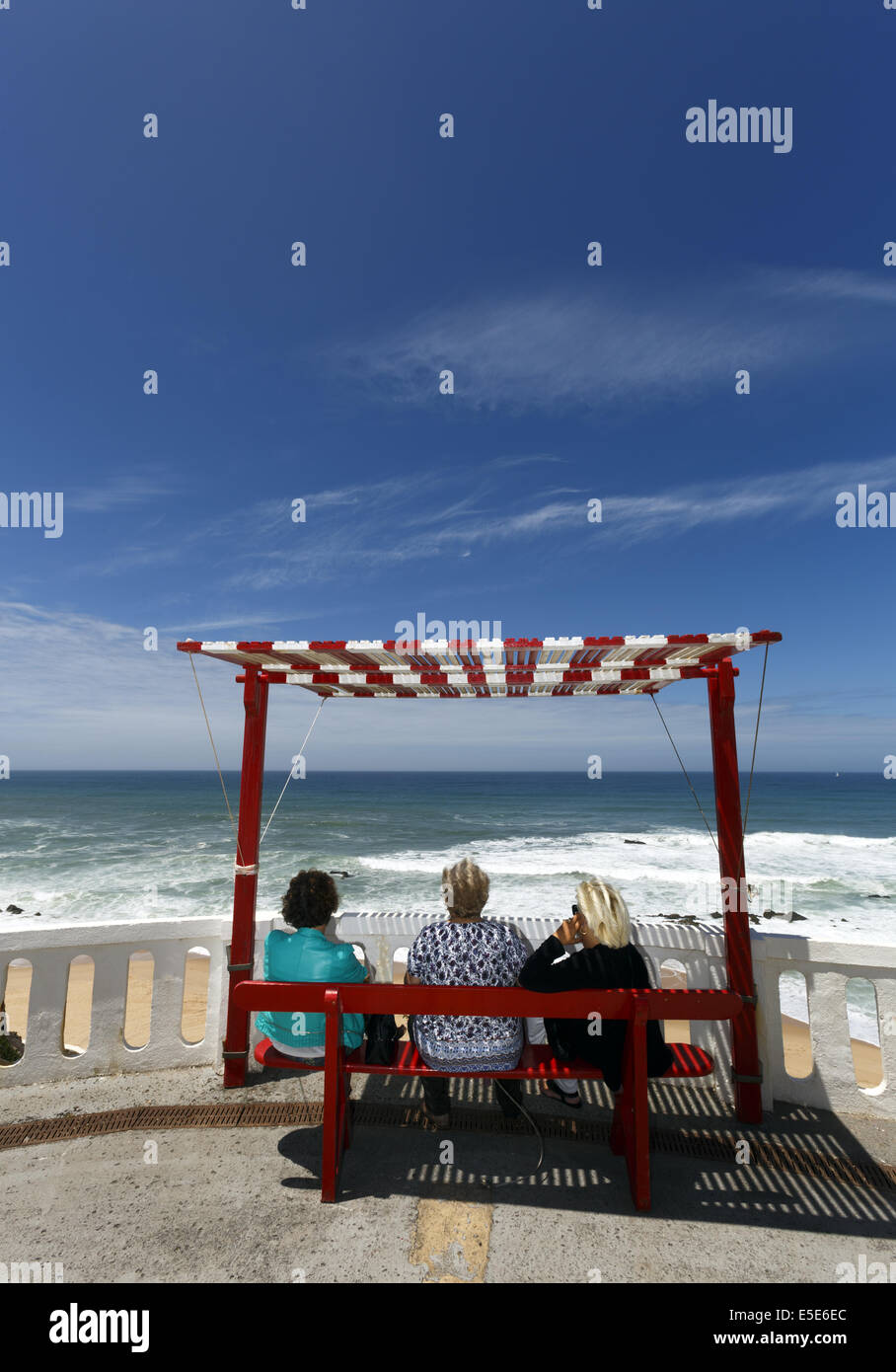Tres mujeres sentadas en un banco de sombra mirando al mar en Silverira, Portugal Foto de stock