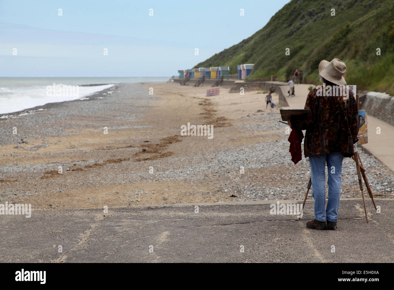 Un solitario pintor con su caballete considera su sujeto, la playa y la costa de Norfolk Foto de stock