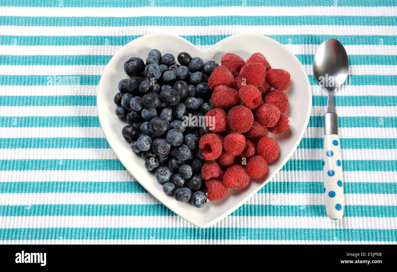 Dieta saludable Una dieta alta en fibra desayuno con arándanos y frambuesas en forma de corazón placa blanca en lugar de banda AQUA BLUE Foto de stock