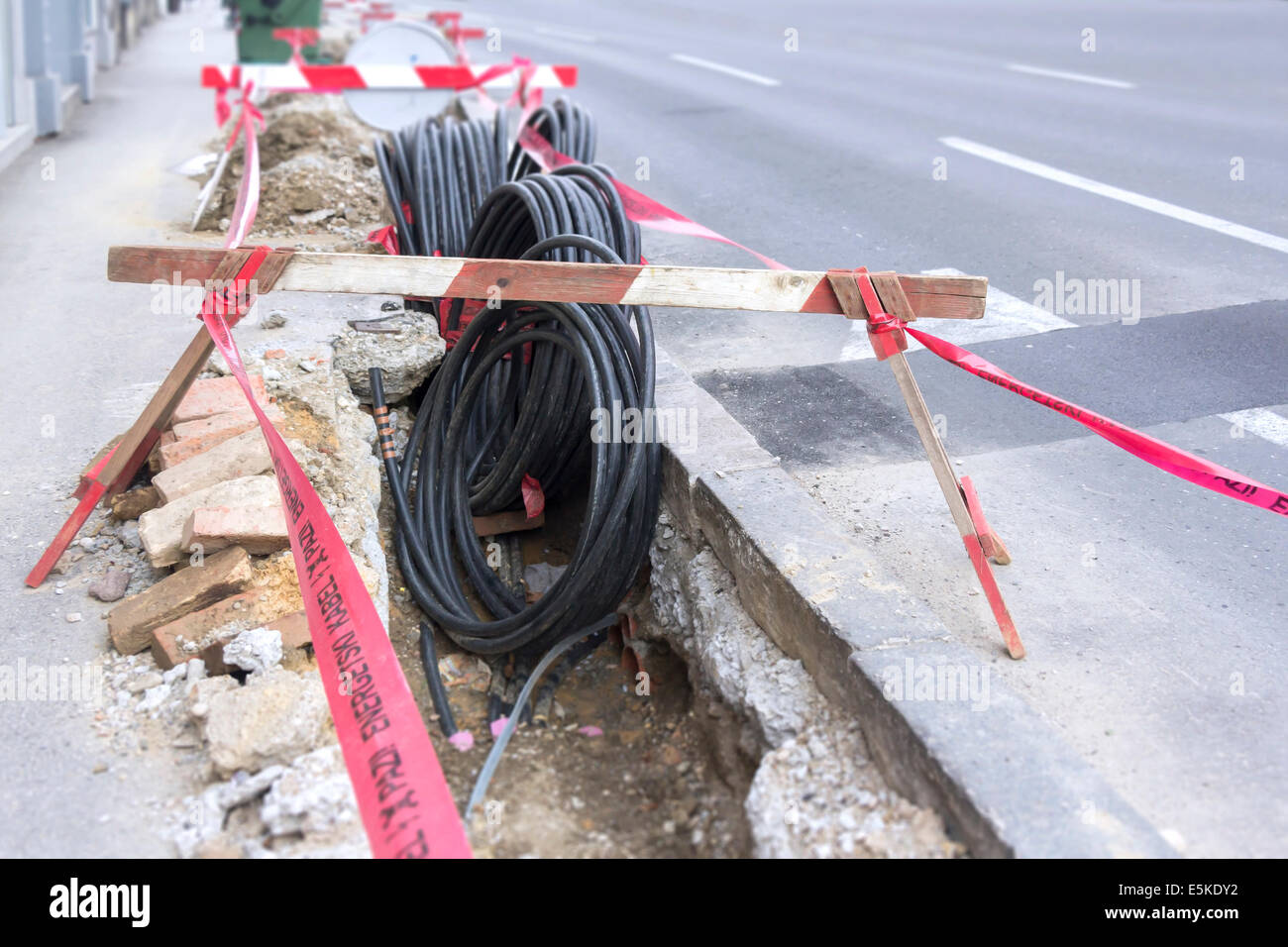 Excavación de carretera en un sitio de construcción en conductos para el tendido de fibra óptica y cable eléctrico Foto de stock